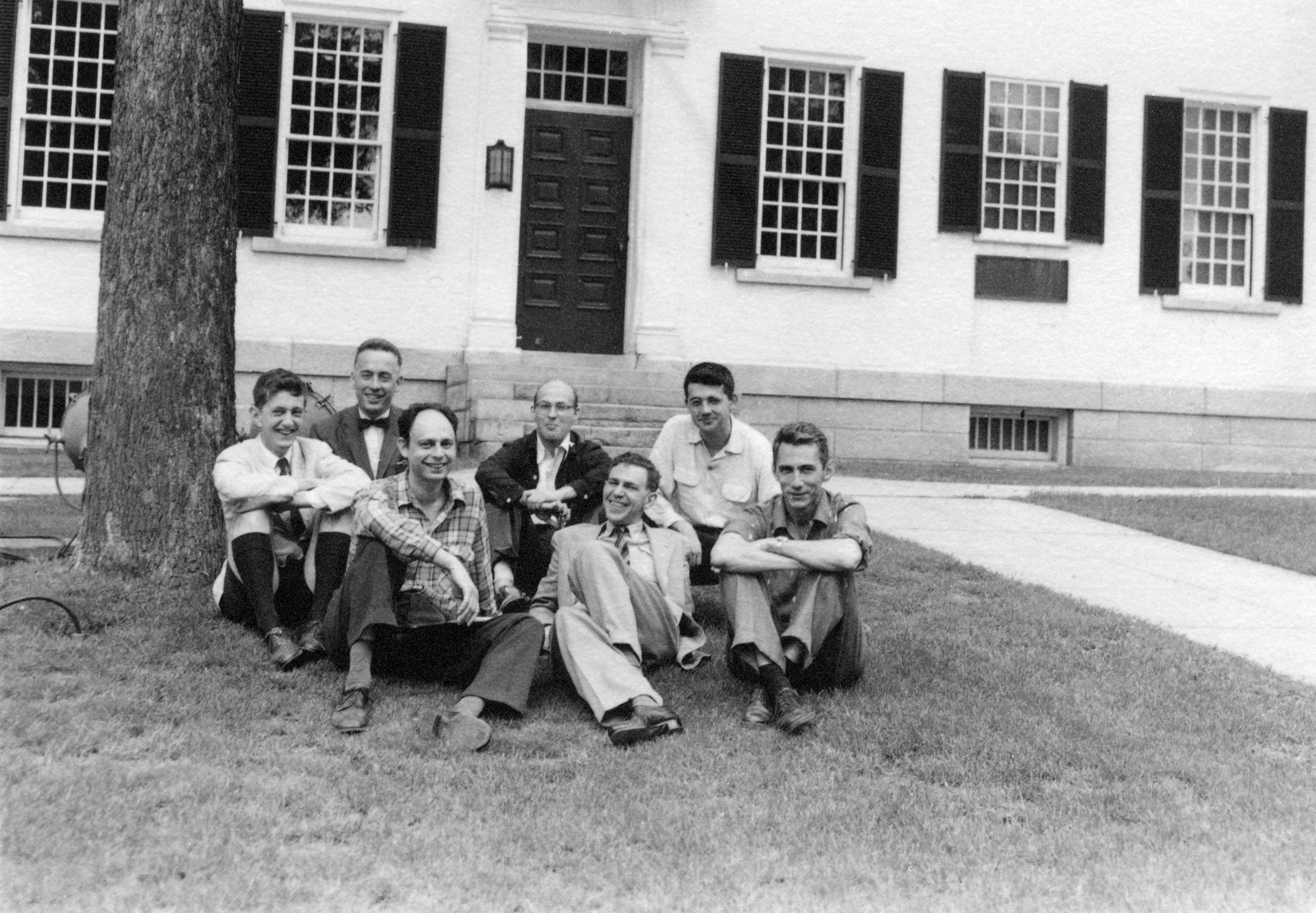 Black and white photo of several men in front of a white building Black and white photo of several men in front of a white building